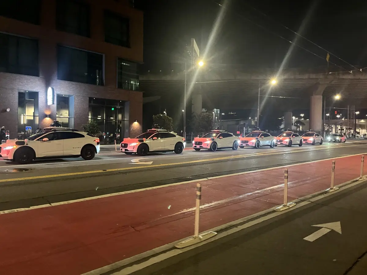 A row of Waymo robotaxis lined up on a San Francisco street at night
