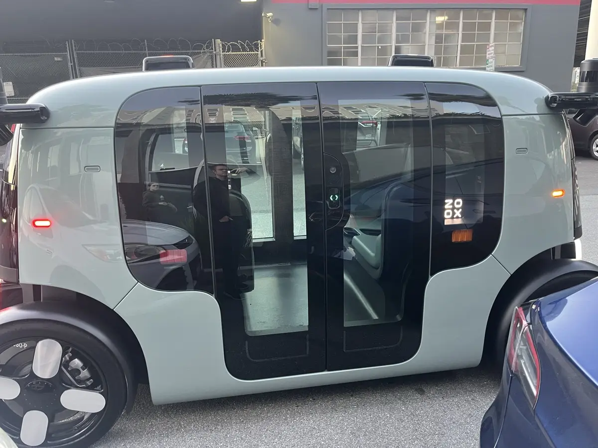 A Zoox robotaxi from the side, showing its symmetric pod design with no steering wheel